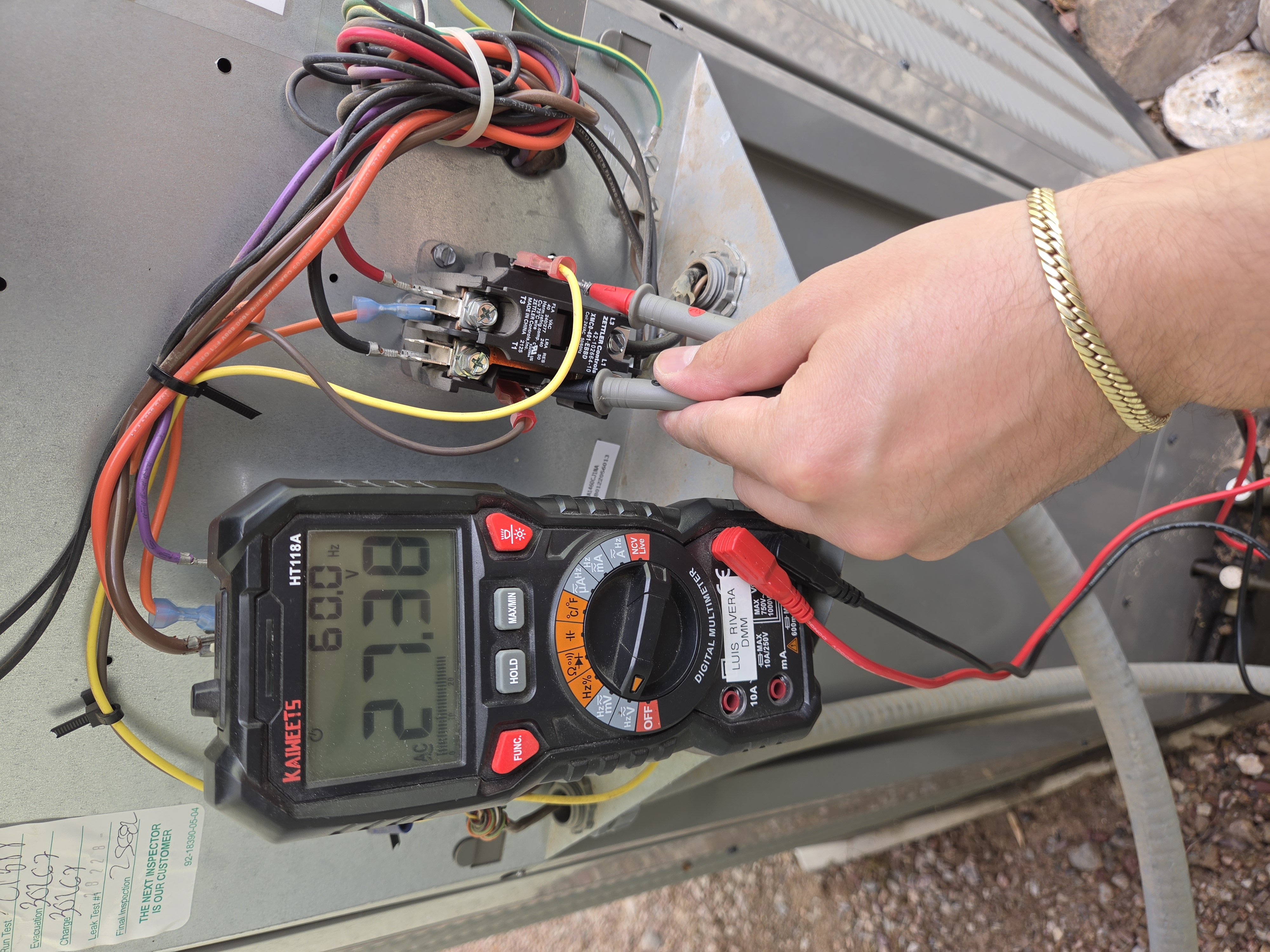 Digital multimeter checking AC thermostat voltage at contactor during service